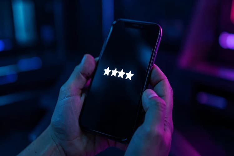 Uma mão segurando um celular exibindo uma avaliação cinco estrelas.